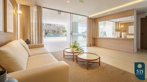 A modern hotel lobby with a sofa, two round tables, a plant, and a reception desk.