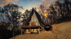 A modern house with a large glass facade, a sloped roof, and a prominent cylindrical structure on the side. - Diamond View PA: A-Frame~Hot Tub~Sauna~Panoramic Mountain Views (Ligonier)