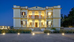 Un grand bâtiment à deux étages, doté d’une façade symétrique, de nombreux balcons et d’une entrée centrale avec des marches.