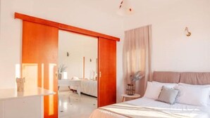 Une chambre à coucher comprenant un lit, une table de chevet, une commode et une porte coulissante donnant sur une salle de bain.