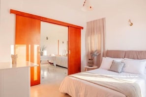Een slaapkamer met een bed, nachtkastje, dressoir en een schuifdeur naar een badkamer.
