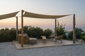 Un área de estar al aire libre con toldo, mobiliario de mimbre y vista al mar.