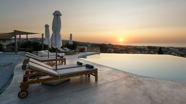 Un espace aménagé au bord de la piscine, avec des chaises longues et des parasols, offrant une vue sur le paysage urbain au coucher du soleil.