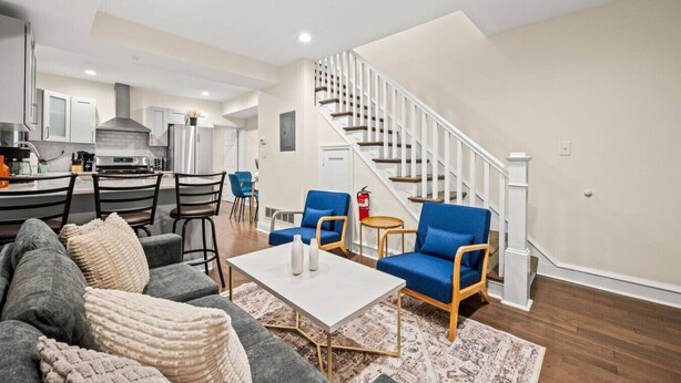 A modern living room with a sofa, coffee table, and blue chairs. There is a staircase with white railings leading to an upper level. - New Spacious 3 Bedroom Apt in the Heart of Philly (Philadelphia)