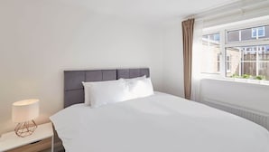 A neatly arranged hotel room with a large bed, a bedside lamp, and a window with curtains.