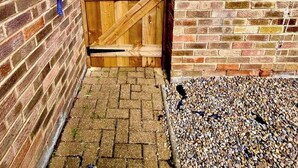 A wooden gate leading to a brick building with a paved entrance area.