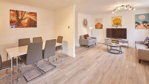 A modern living room with a dining area, a sofa, a TV, and artwork on the walls.