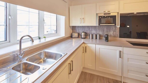 A modern kitchen with white cabinets, stainless steel appliances, and a large window providing natural light.