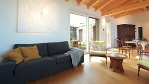 A modern living room with a grey sofa, wooden flooring, and a dining area with a table and chairs. - Casa Delle Eriche, Colli Euganei, Pool, Wifi (Teolo)