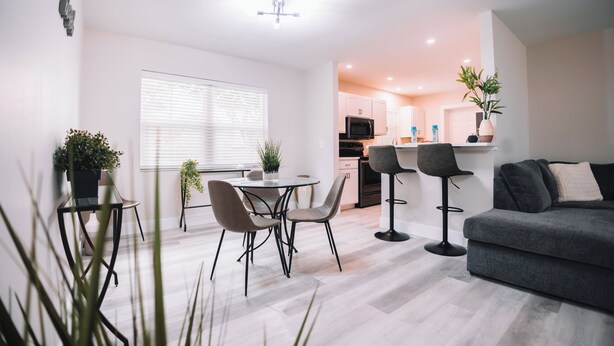 A modern living room with a grey sofa, a dining table with chairs, and a kitchen area in the background. - A Modern Beach Concept - Re:Treat 408 (Bradenton)