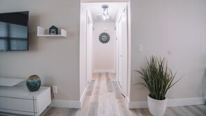 A hallway with a flat-screen TV, a decorative vase, a potted plant, and a mirror on the wall. - A Modern Beach Concept - Re:Treat 408 (Bradenton)