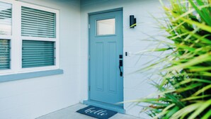 A blue door with a small window, a doormat with the word "hello," and a wall-mounted light fixture. - A Modern Beach Concept - Re:Treat 408 (Bradenton)