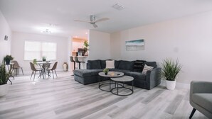 A modern living room with a grey sofa, a coffee table, and a dining area with chairs and a table. - A Modern Beach Concept - Re:Treat 408 (Bradenton)