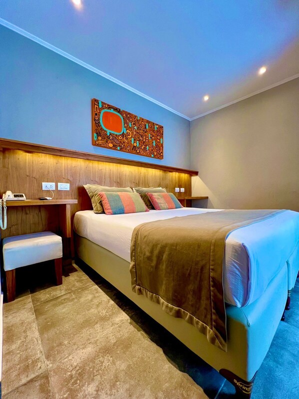 A hotel room with a large bed, a wooden headboard, a bedside table with a lamp, and a wall-mounted artwork. - Romina Art Hotel (Villa Gesell)