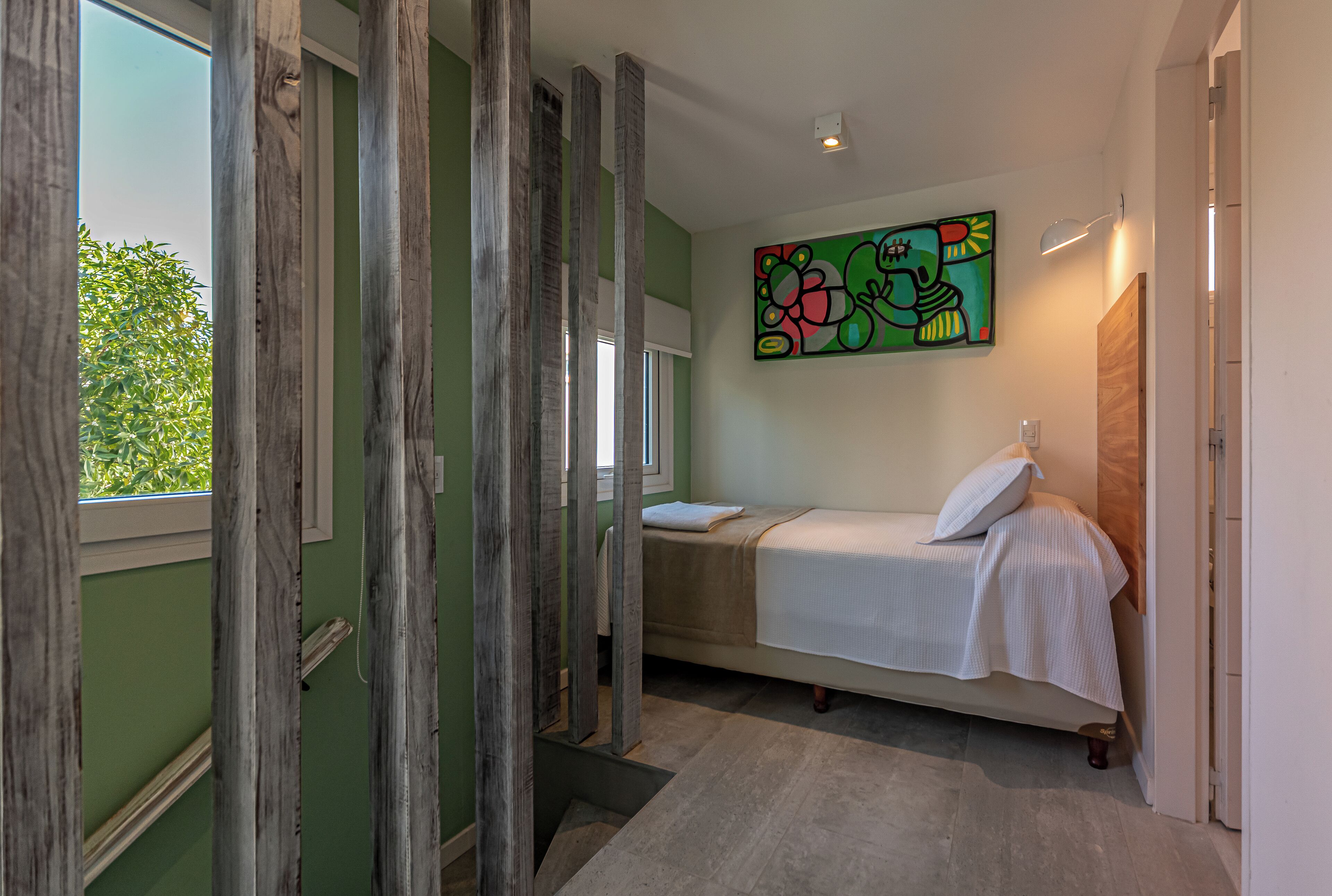 A bedroom with a bed, a window, and a colorful abstract painting on the wall.