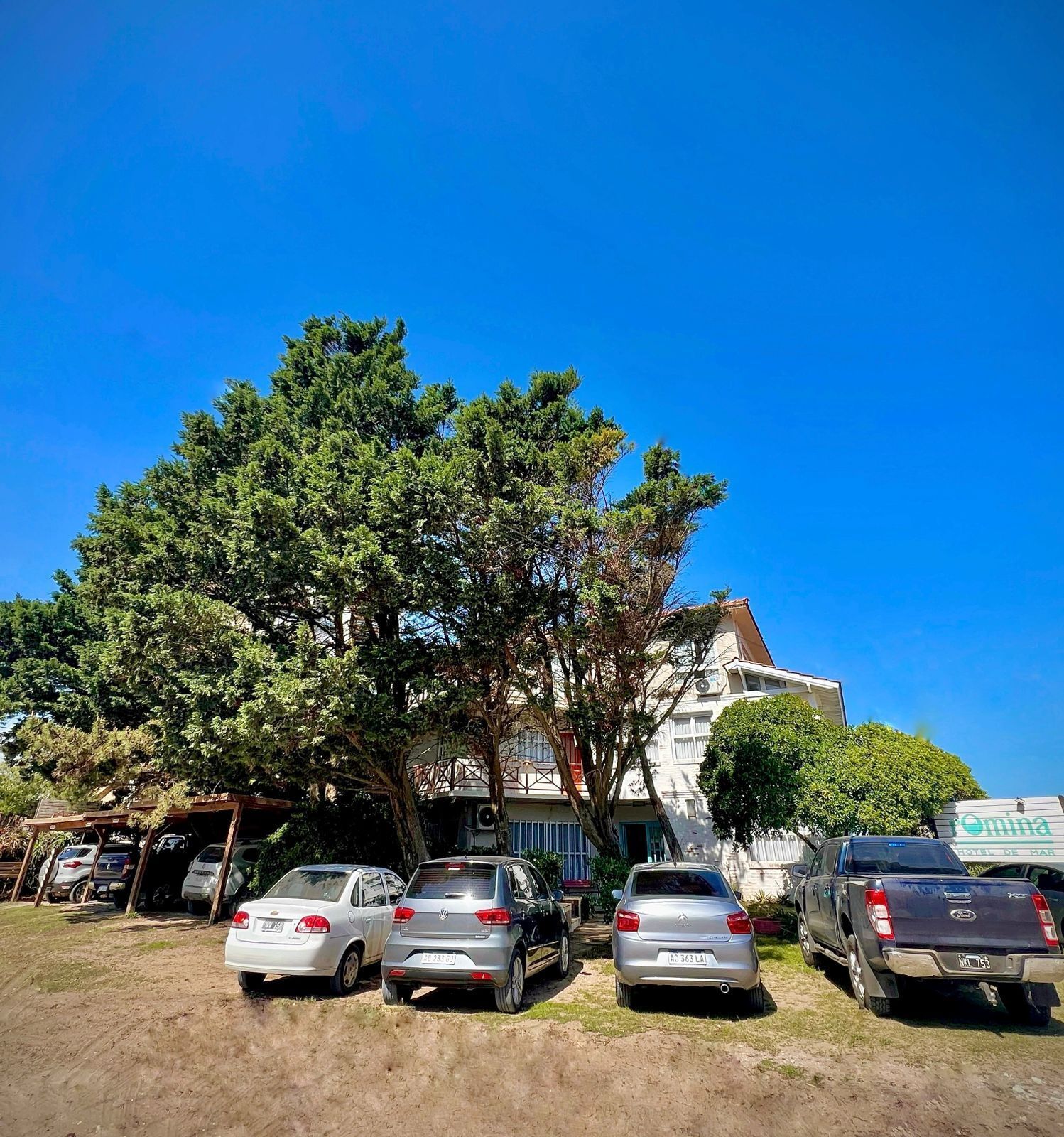 A parking area with several cars, a large tree, and a building with a sign that reads "OMINA HOTEL DE PARIS".