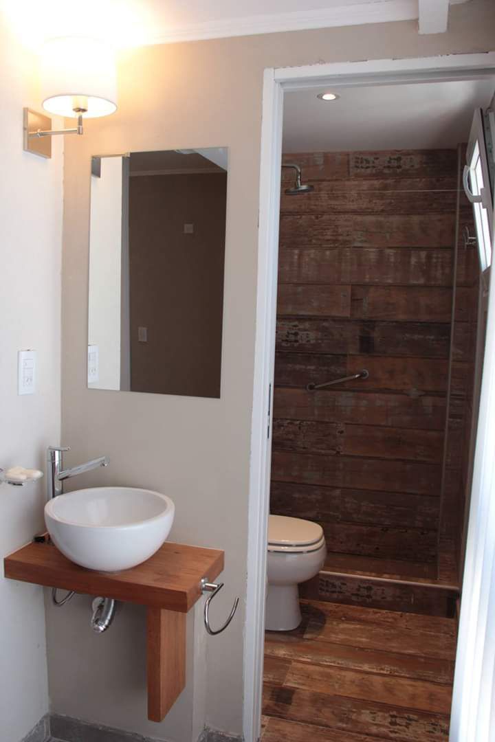 A bathroom with a wooden vanity, a white sink, a mirror, and a shower with wooden walls.