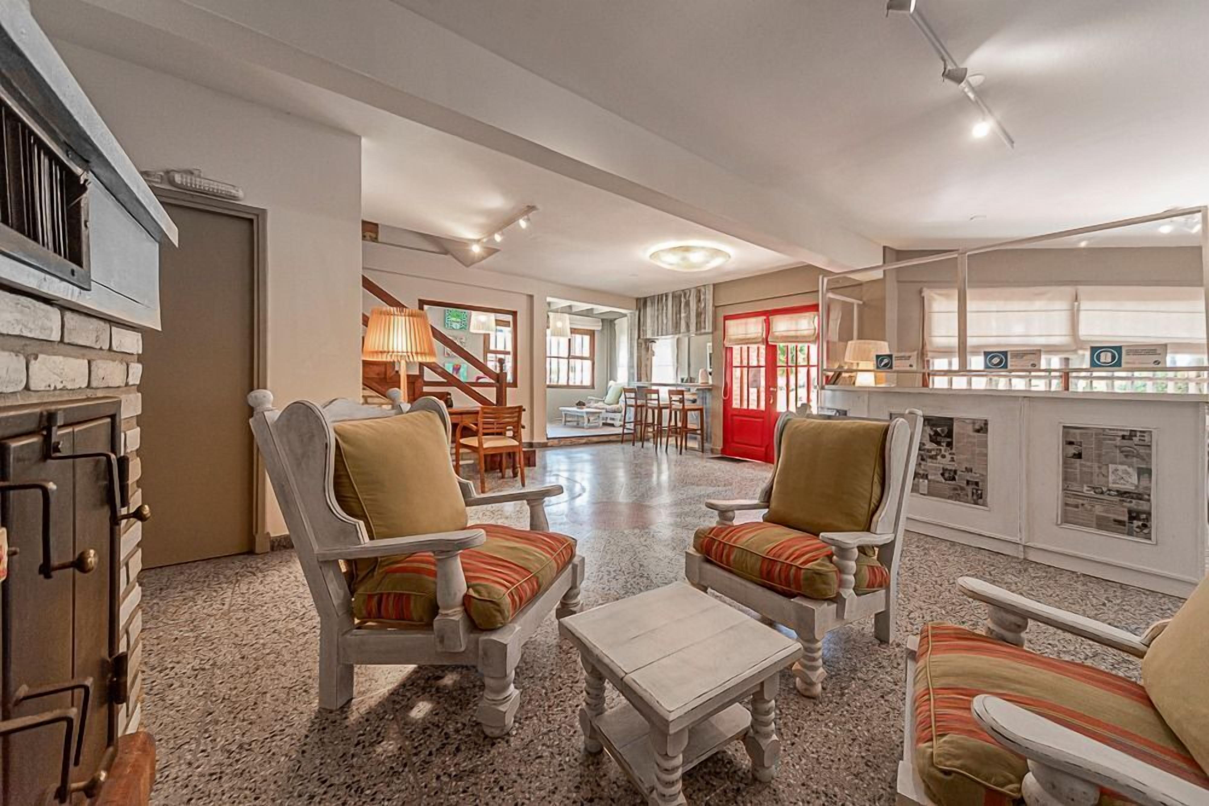 A spacious living area with a fireplace, two armchairs with striped cushions, a coffee table, and a kitchen area with a red door.
