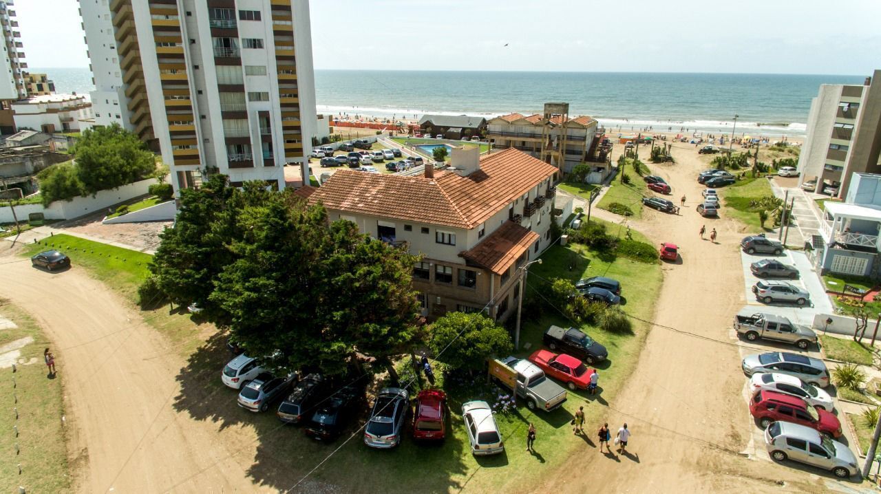 A coastal residential area with a multi-story building, a parking lot, and a beach in the background.