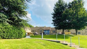 A courtyard with stone buildings, a grassy area, and a metal railing. - Cosy Cottage in South Yorkshire Village. 
 (Darfield)