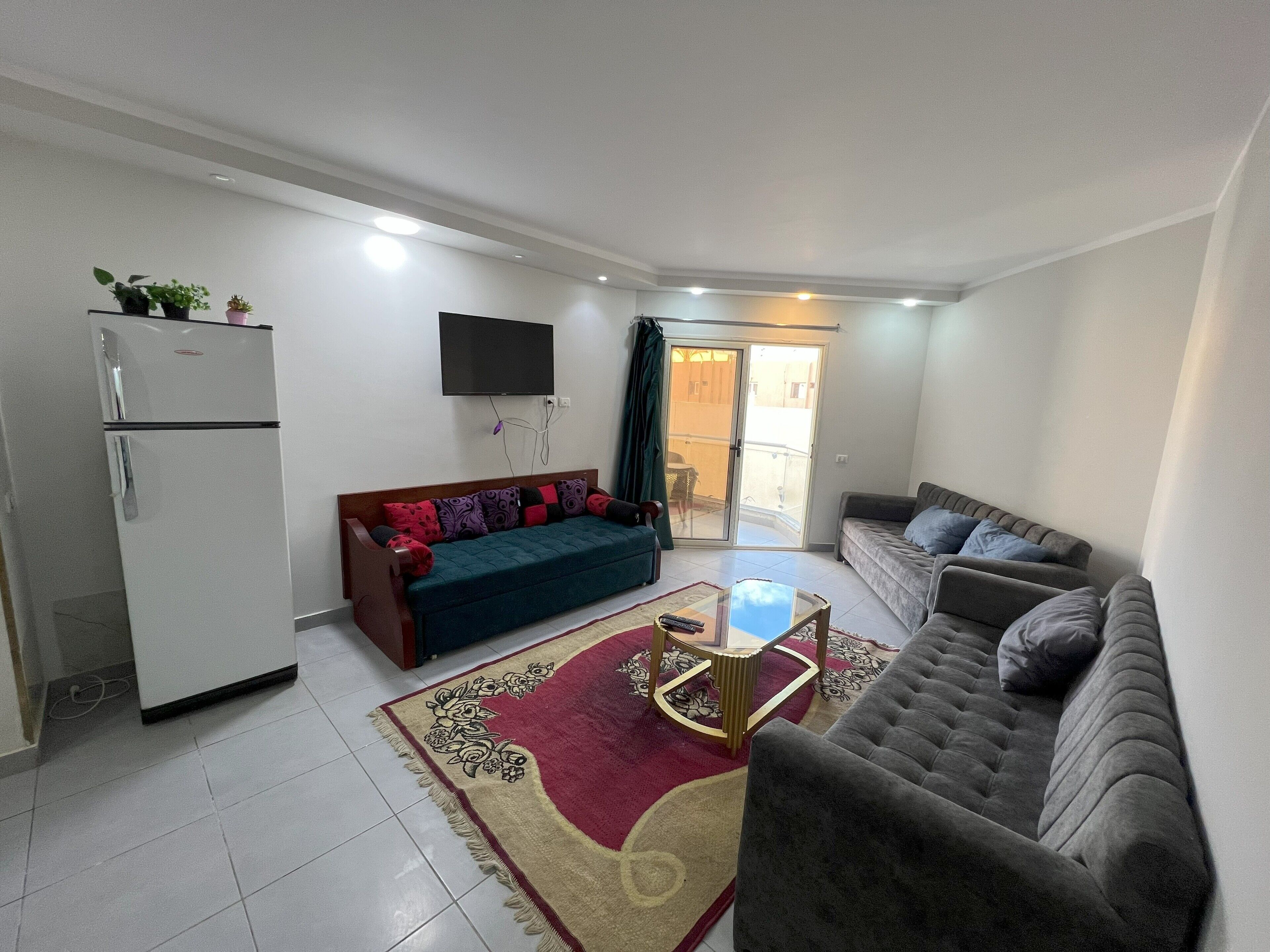 Una sala de estar con un sofá, una mesa de centro y un televisor. Hay una puerta corrediza que da a un área exterior.