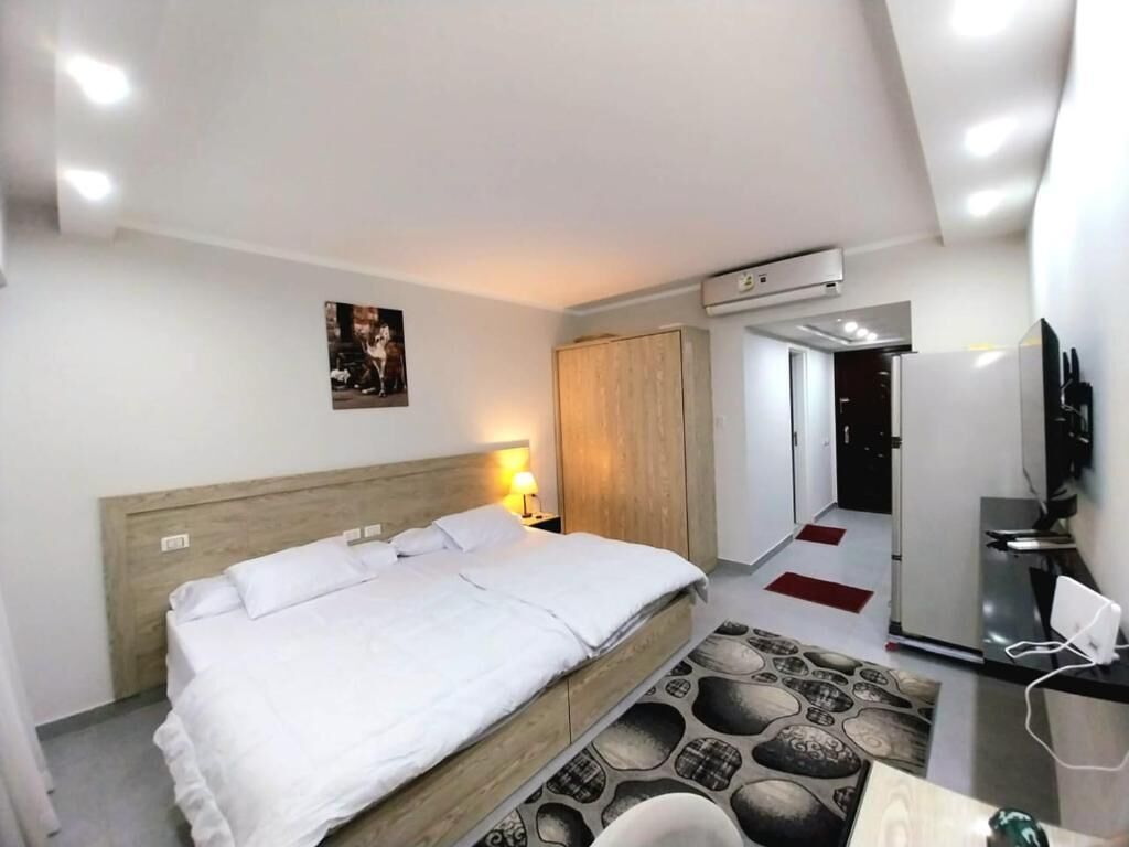 A modern hotel room with a large bed, a desk with a chair, a TV, and an air conditioning unit.