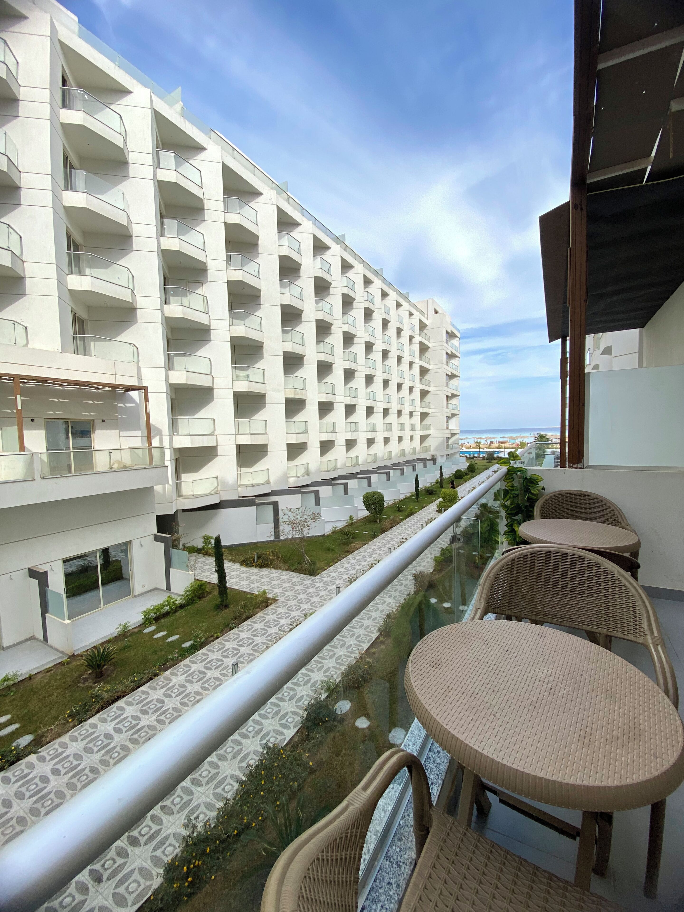 Een modern hotel met een lang balkon, rieten meubilair en uitzicht op het strand.