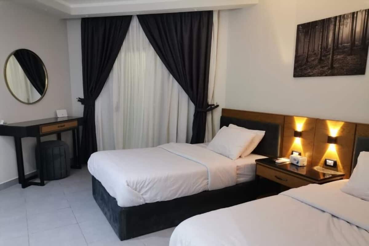 A hotel room with two beds, a desk, a mirror, and a painting on the wall.