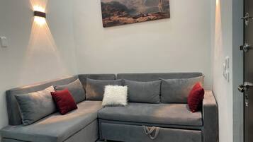 A grey sectional sofa with red and white cushions, a painting above it, and a wall-mounted light fixture.