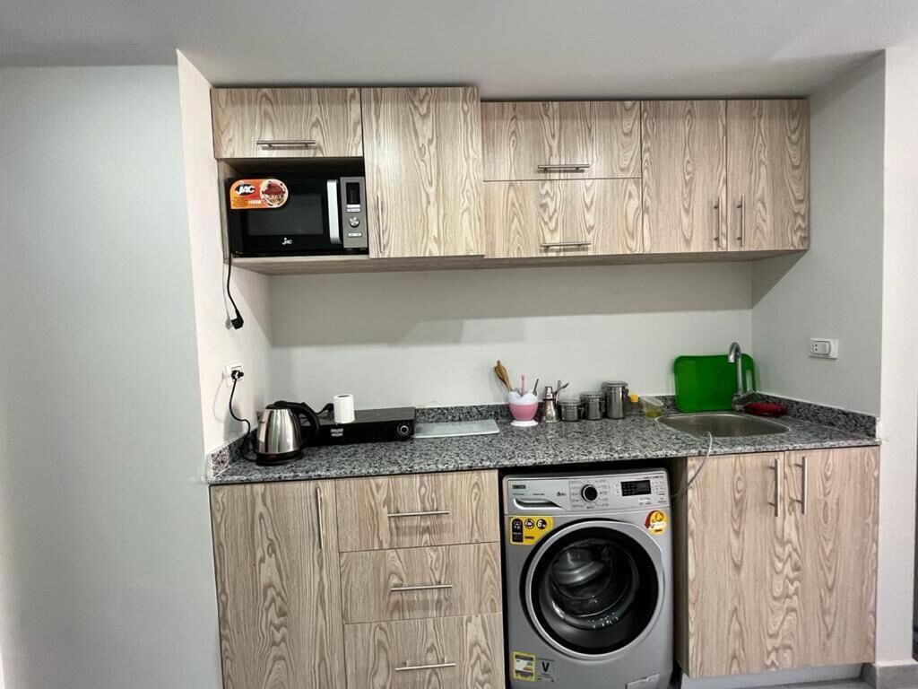 A compact kitchen with wooden cabinets, a built-in microwave, a washing machine, and a granite countertop.