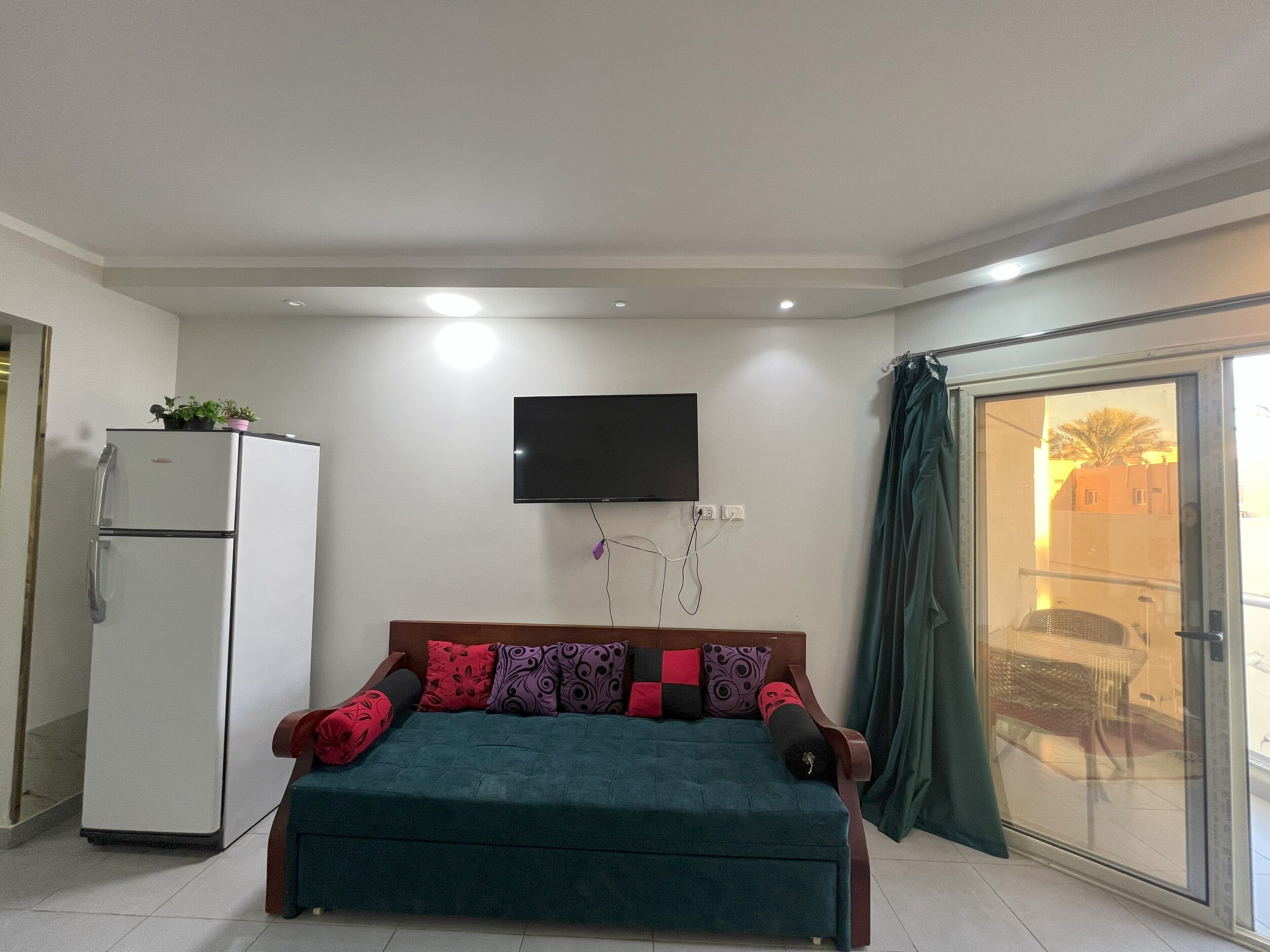 Una habitación con cama, televisión montada en la pared y puerta corrediza de vidrio que da a un espacio exterior.