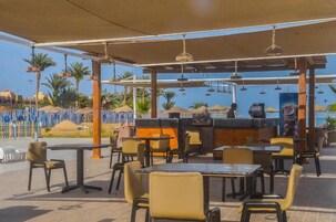 An outdoor dining area with tables and chairs, a bar, and a view of palm trees and buildings.