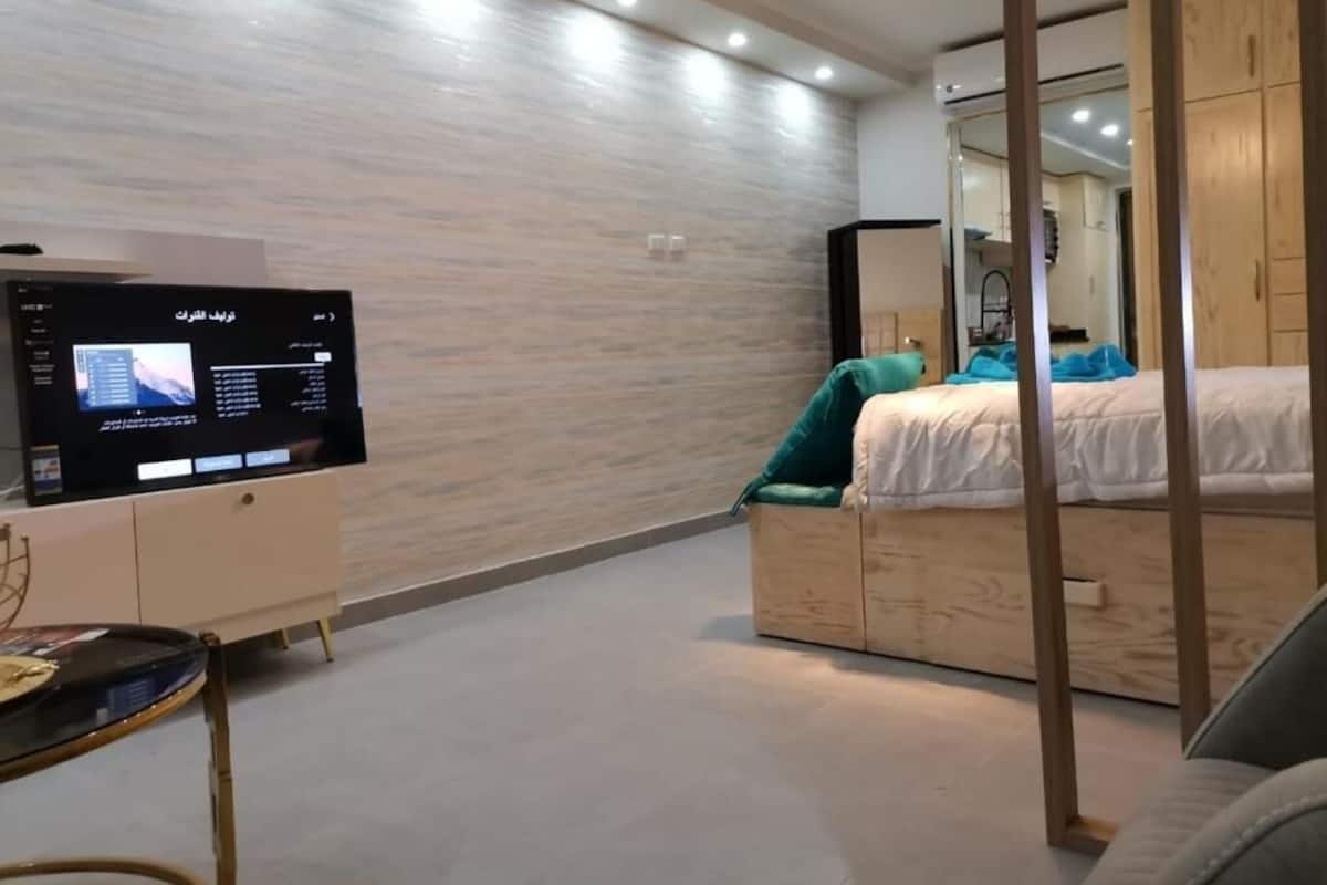 A modern bedroom with a bed, a TV on a stand, and a wooden wardrobe.