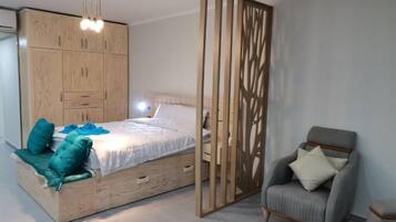 Un dormitorio con cama, armario de madera, sillón gris y un separador decorativo.