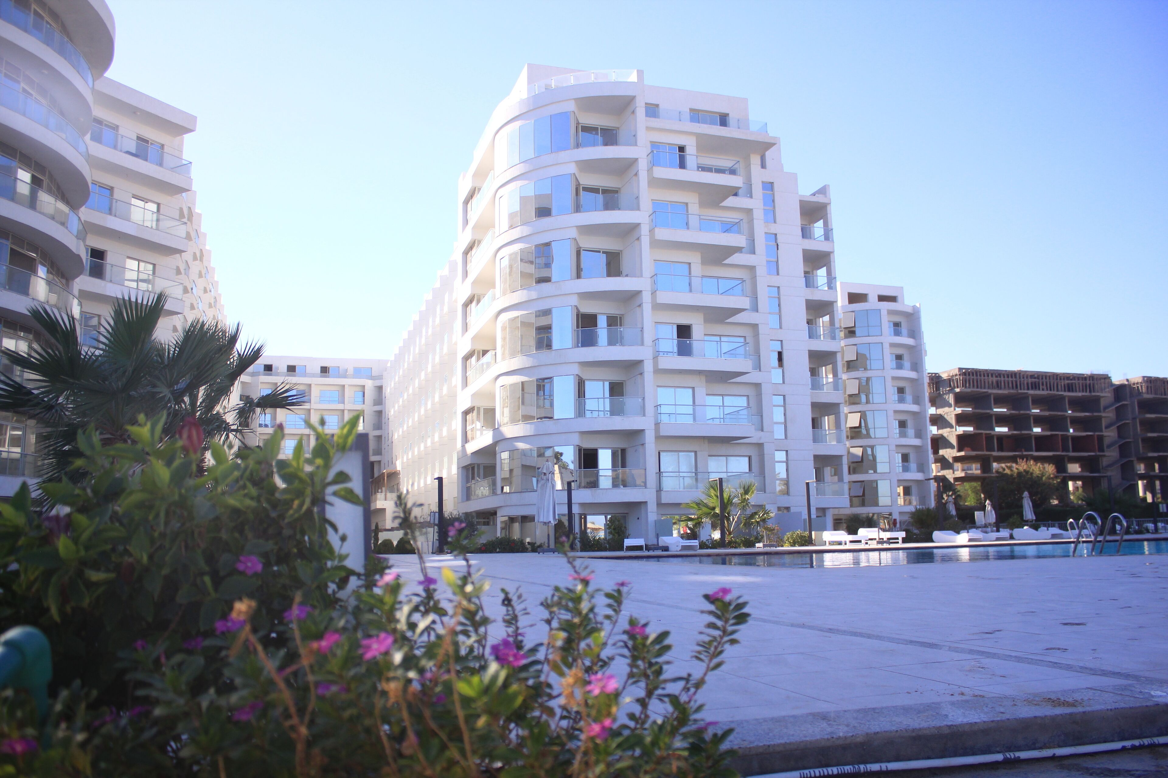 A modern multi-story hotel with balconies, a swimming pool, and surrounding greenery.