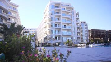 A modern multi-story hotel with balconies, a swimming pool, and surrounding greenery.
