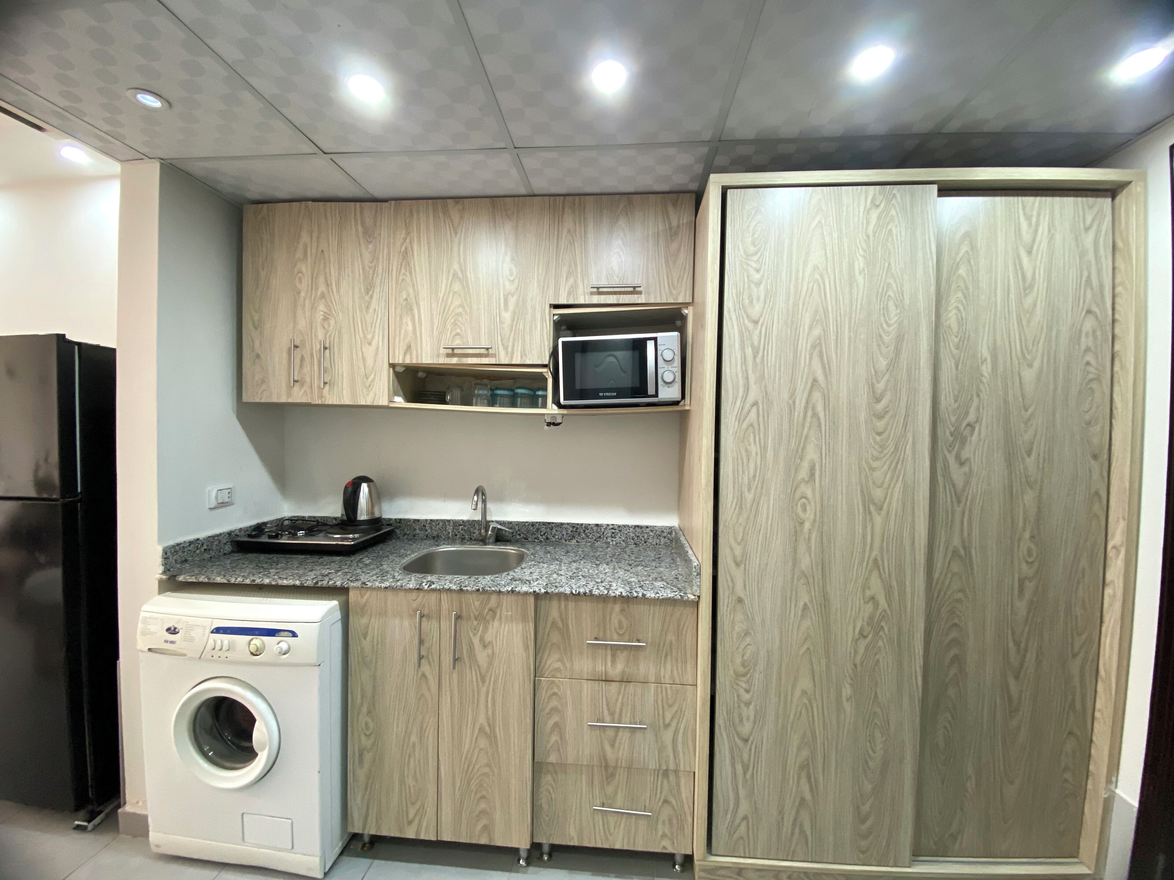 A compact kitchen with wooden cabinets, a microwave, a sink, and a washing machine.