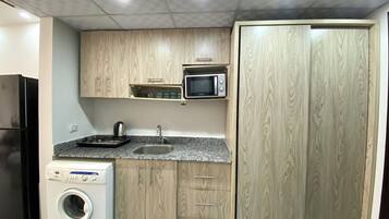 A compact kitchen with wooden cabinets, a microwave, a sink, and a washing machine.