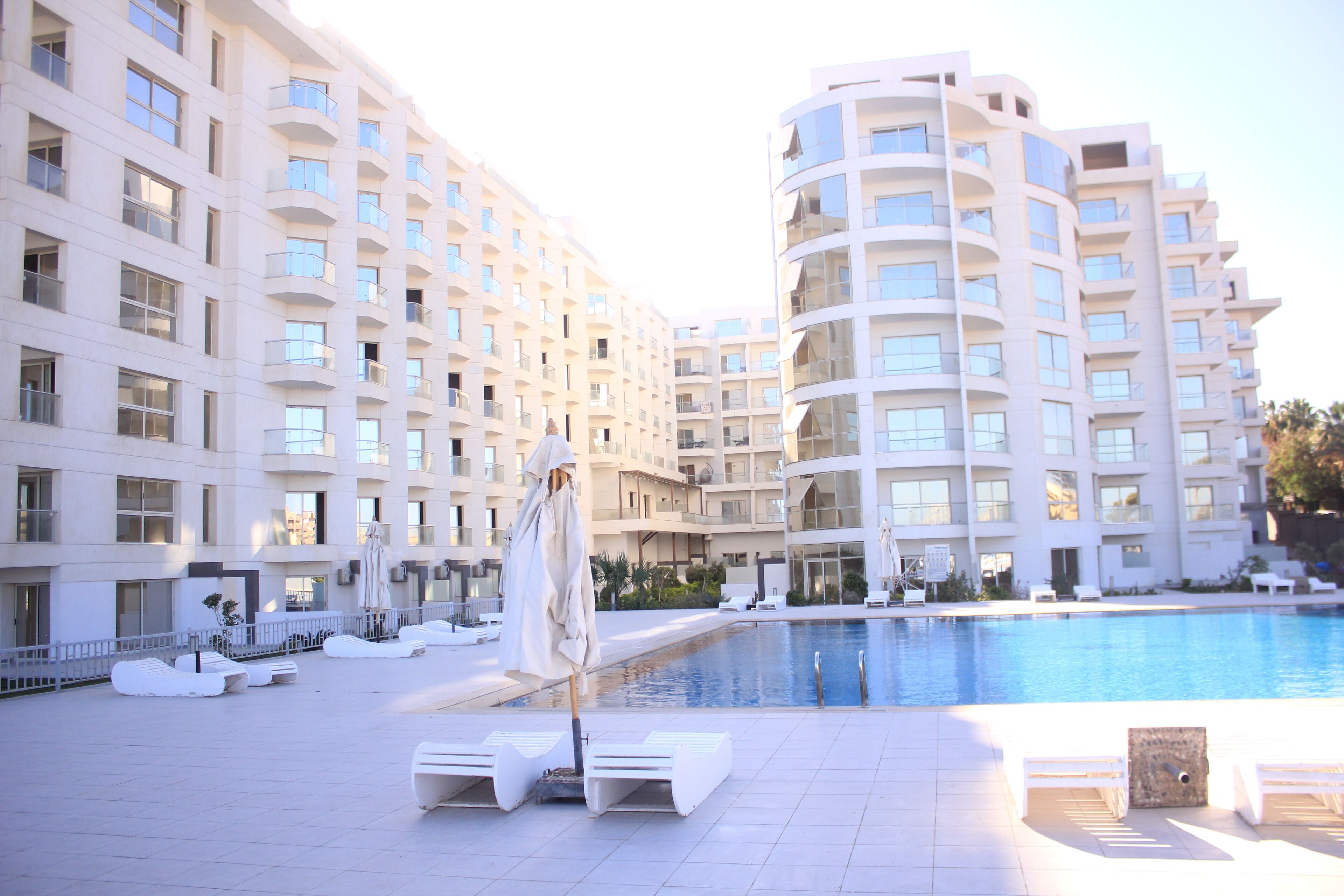 A modern hotel with a large pool, white balconies, and sun loungers.