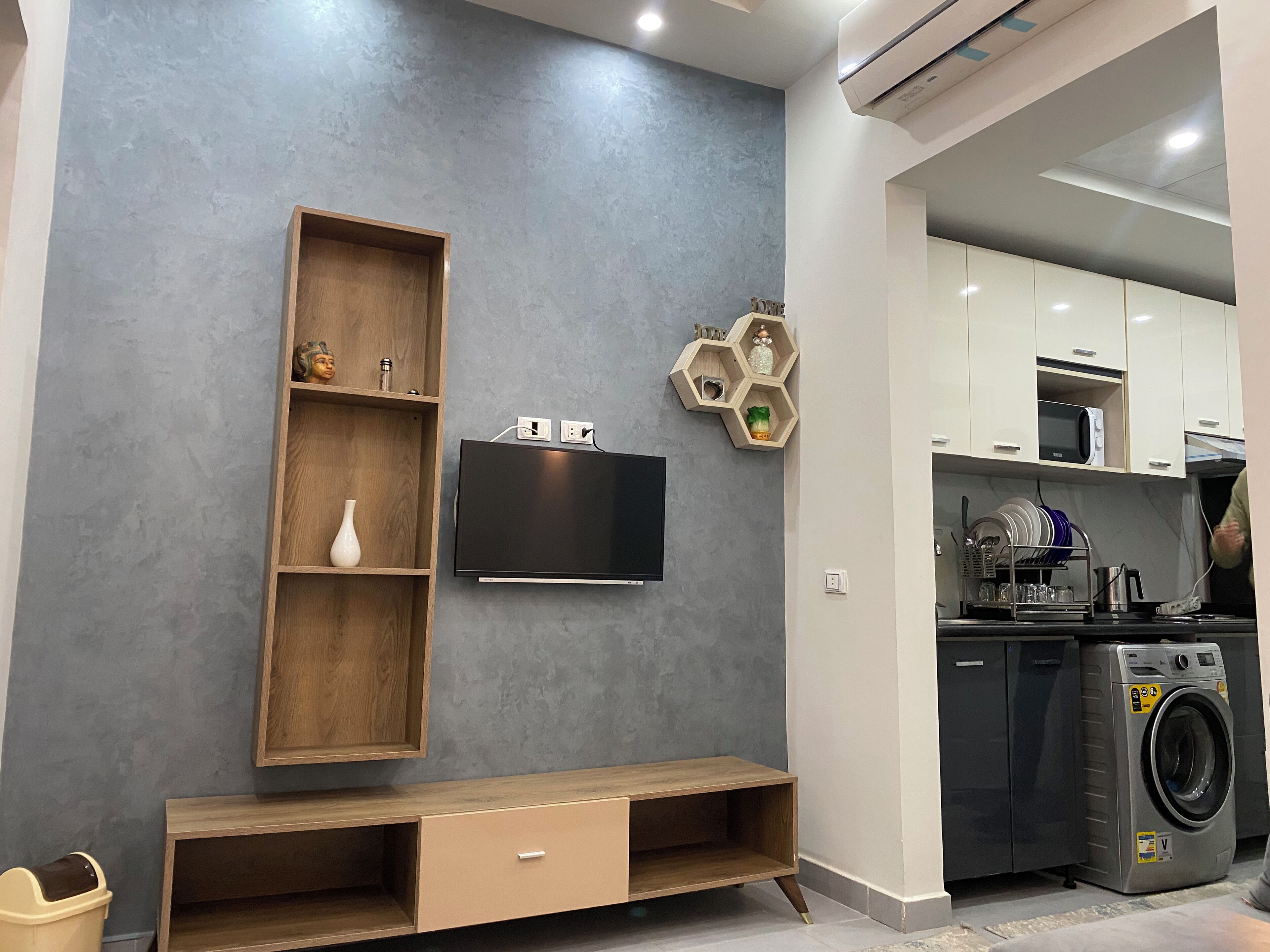 Een moderne keuken met inbouwapparatuur, een flatscreen televisie, houten planken en een wasruimte.