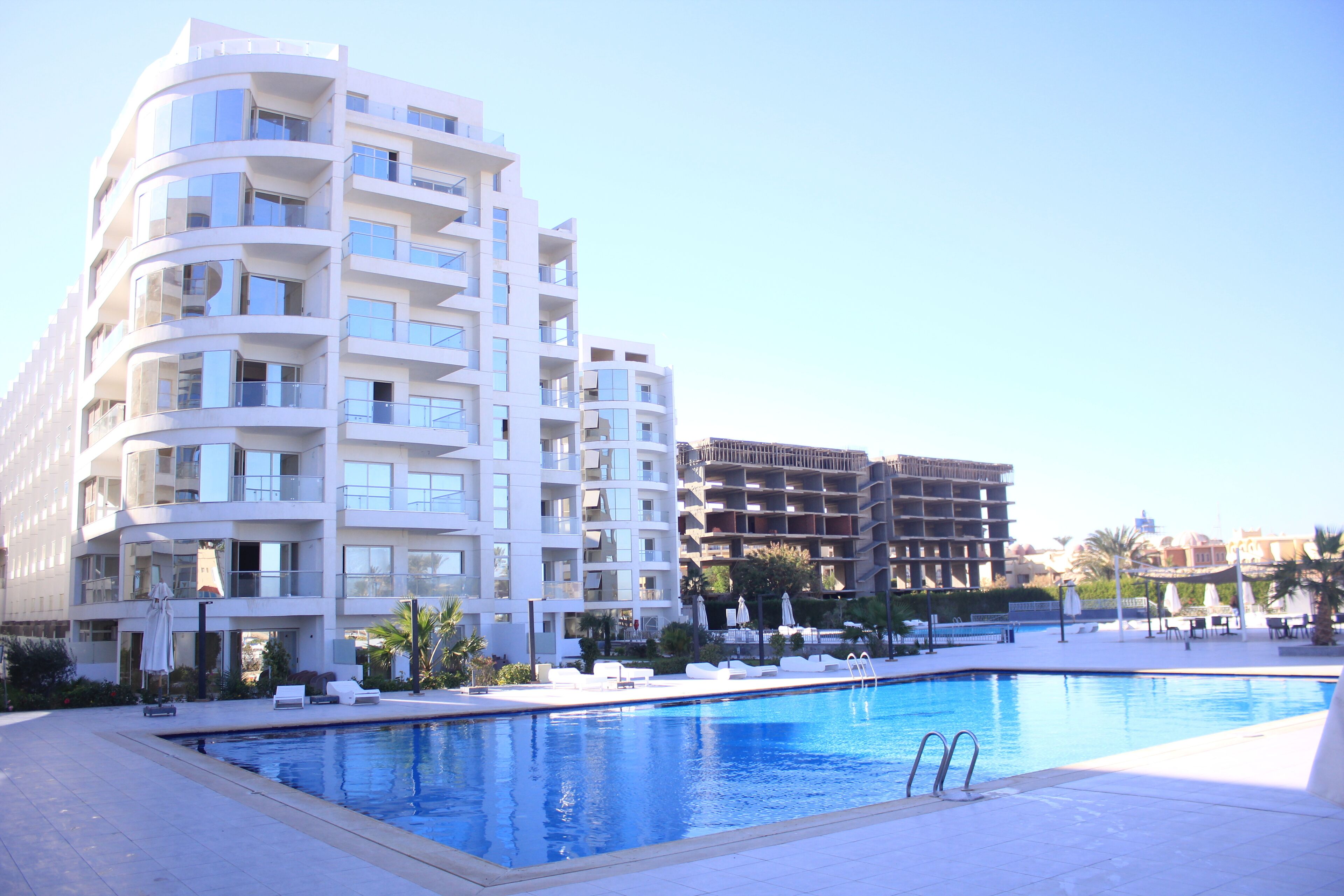 A modern hotel with a swimming pool, multiple balconies, and outdoor seating areas.
