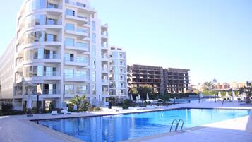 A modern hotel with a swimming pool, multiple balconies, and outdoor seating areas.