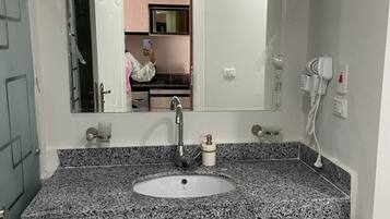 A bathroom with a granite countertop sink, a large mirror, and a hairdryer on the wall.