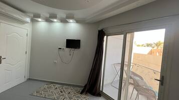 Habitación de hotel con un gran ventanal corredera a un balcón, un televisor de pantalla plana en la pared y una alfombra estampada en el suelo.