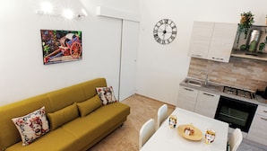A modern kitchen with a white countertop, a stove, and a sink. There is a dining table with chairs and a sofa with decorative pillows. - Entire apartment in the center of Palermo (Palermo)