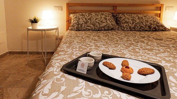 A neatly made bed with a patterned bedspread, a tray with cookies and two cups, and a small table with a lamp and a plant. - Entire apartment in the center of Palermo (Palermo)