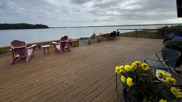 A wooden deck with Adirondack chairs, a table, and a potted plant with yellow flowers. - Picturesque Family-Friendly Beach Home! Sunrises @ Sandy Point (Ferndale)