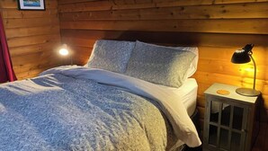 A wooden cabin bedroom with a bed, pillows, a nightstand with a lamp, and a framed picture on the wall. - Picturesque Family-Friendly Beach Home! Sunrises @ Sandy Point (Ferndale)