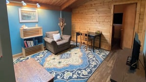 A cozy room with a wooden ceiling, a blue wall, a patterned rug, a sofa, a small table, a bookshelf, and a door leading to another room. - Picturesque Family-Friendly Beach Home! Sunrises @ Sandy Point (Ferndale)
