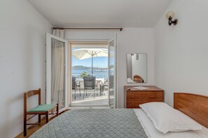 A bedroom with a bed, a wooden dresser, a chair, and a sliding glass door leading to a balcony with a table and chairs. - Seafront apartments Marija with terrace and mooring (Rogoznica)